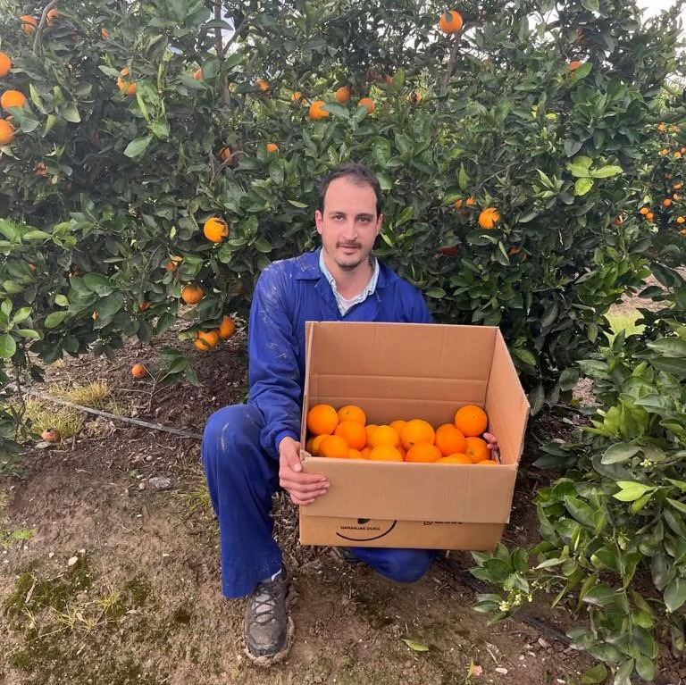 Nando Dura holding a box of oranges in his farm