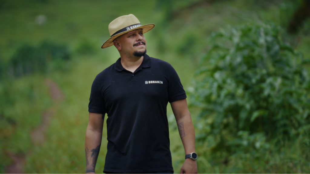 Talles Carvalho walks through the coffee farm wearing a Bonanza hat and shirt